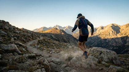 Coureur de trail courant sur un sentier de montagne rocheux avec panorama sur les sommets au lever du soleil